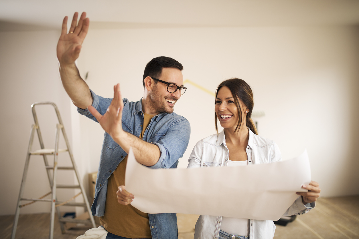 Young couple standing in their apartment while woman holding blueprint and man showing to her new ideas.